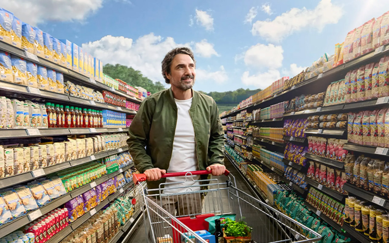 Person im Supermarkt zwischen zwei Regalgängen mit Einkaufswagen voller Lebensmittel
