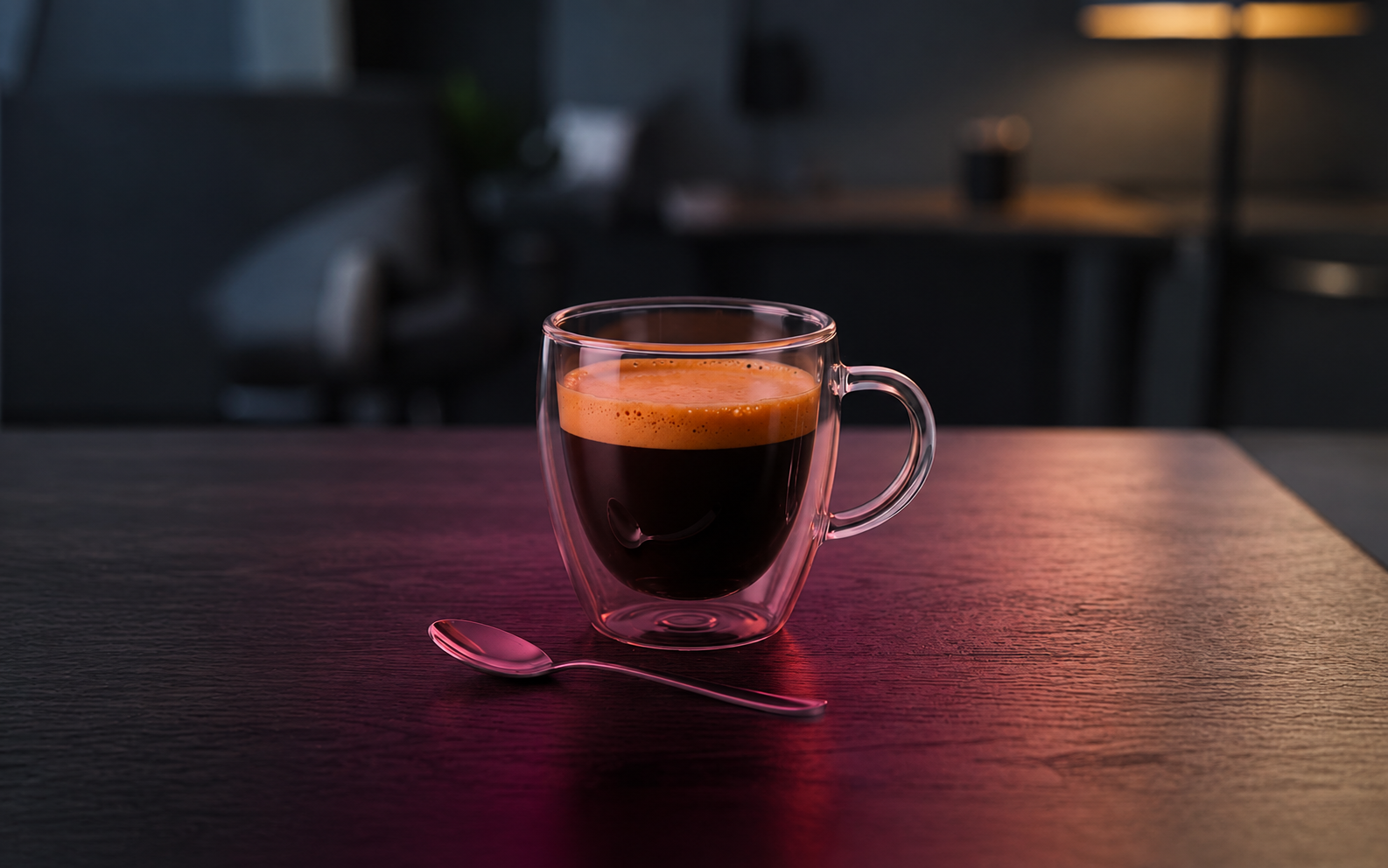 Glastasse mit dunklem Kaffee und Schaumkrone auf einem Holztisch, daneben ein Löffel, warm beleuchtet.